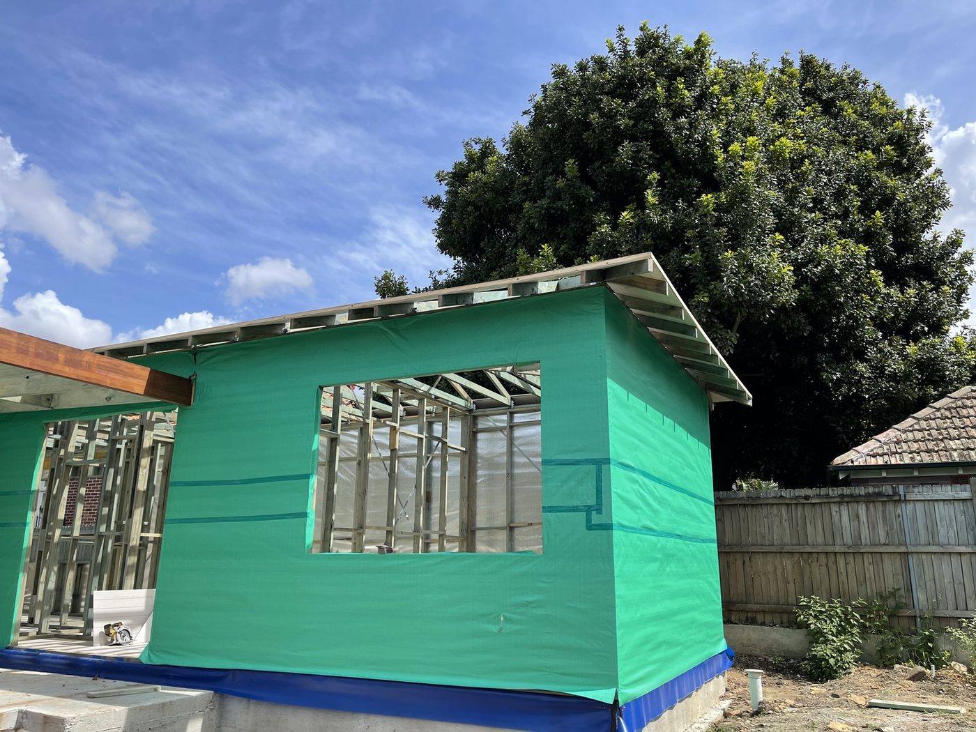 Addition wrapped in green building wrap with window openings and skillion eaves, weathertight stage, Ashfield by Loel Homes