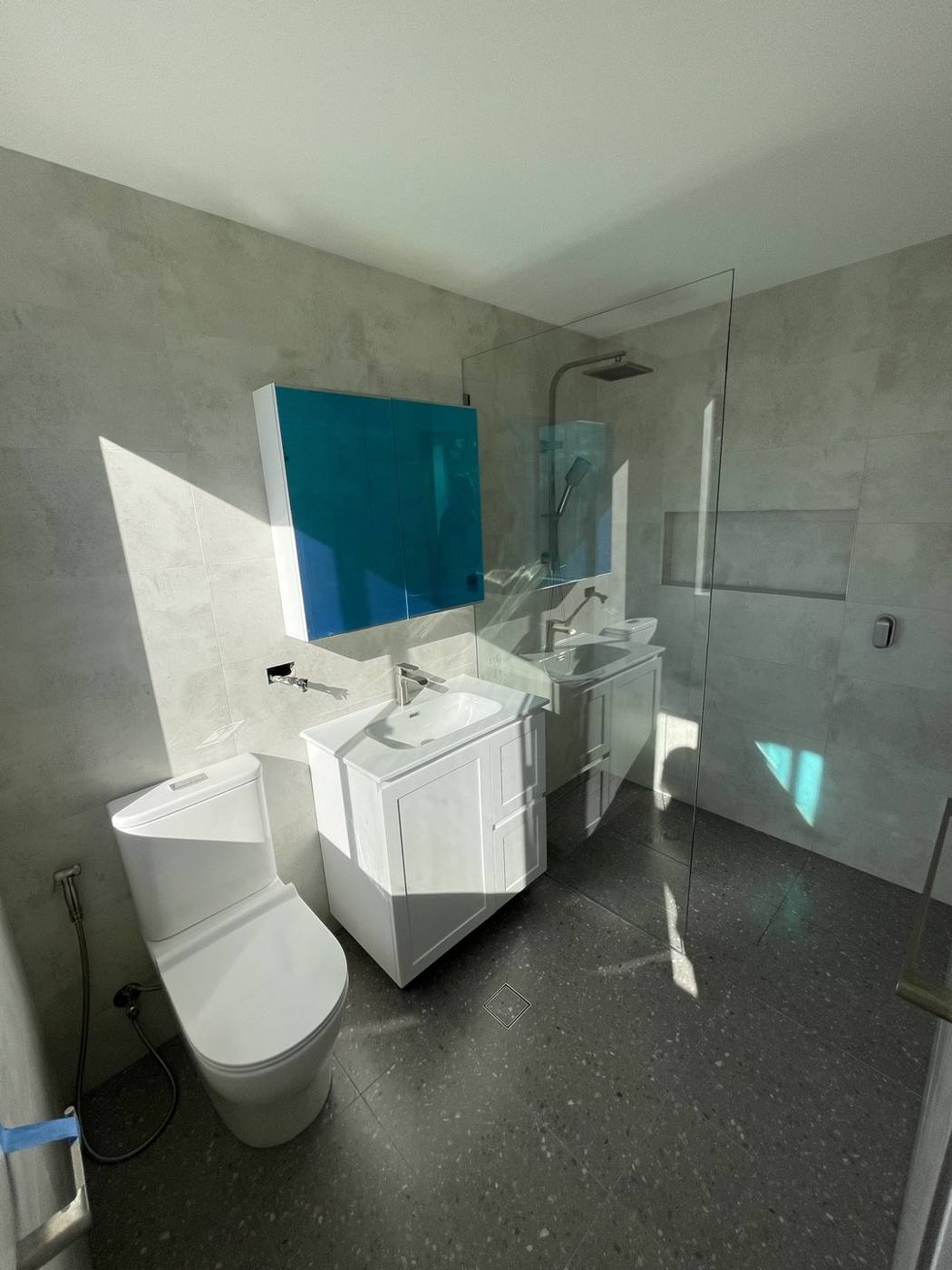 Finished bathroom after renovation with white shaker vanity, teal gloss mirror cabinet, new toilet and frameless walk-in shower on concrete-look tiles, Baulkham Hills by Loel Homes