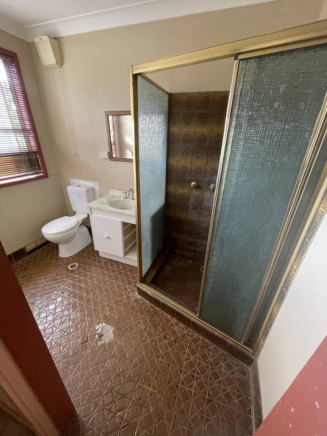 Dated original bathroom before renovation with brown patterned floor tiles, brass sliding shower screen and old vanity, Baulkham Hills by Loel Homes