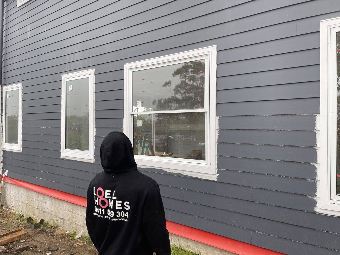 Loel Homes team member reinstating navy weatherboard cladding around the relocated windows, by Loel Homes