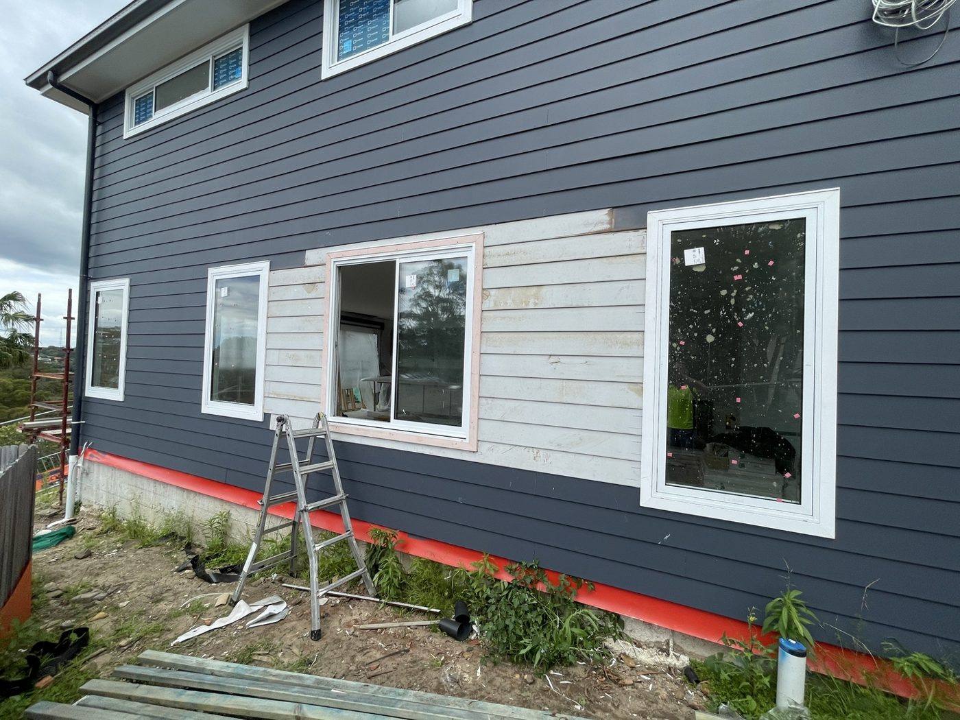 Wider view of navy weatherboard wall with wrapped section where boards are being blended back in, by Loel Homes