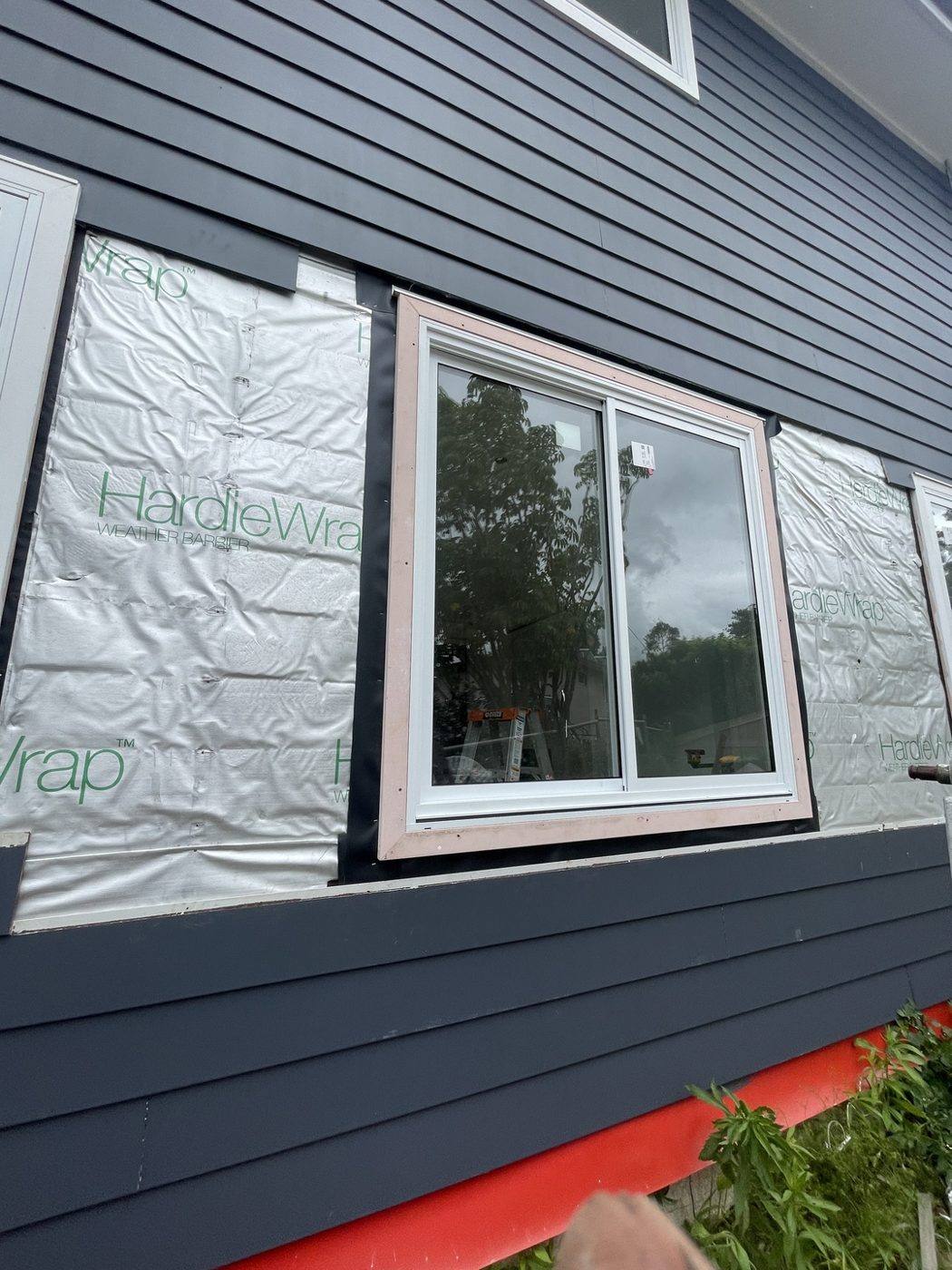 Relocated window installed in navy weatherboard wall with HardieWrap exposed around the new opening, by Loel Homes
