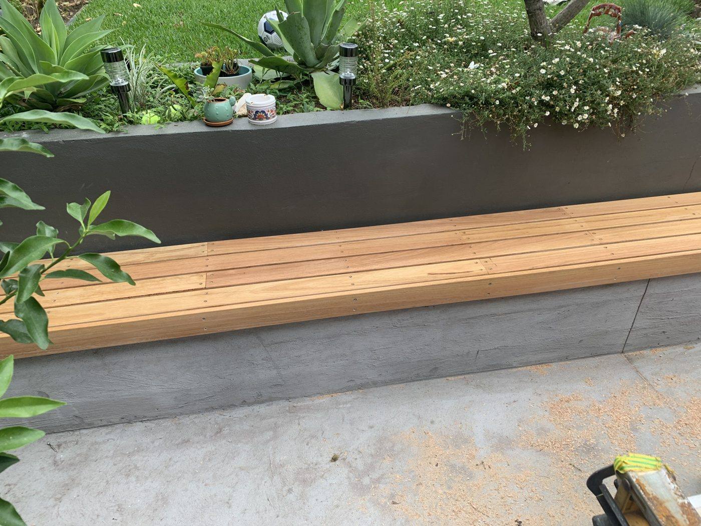 Built-in timber bench beneath a charcoal rendered planter wall filled with greenery in a courtyard by Loel Homes