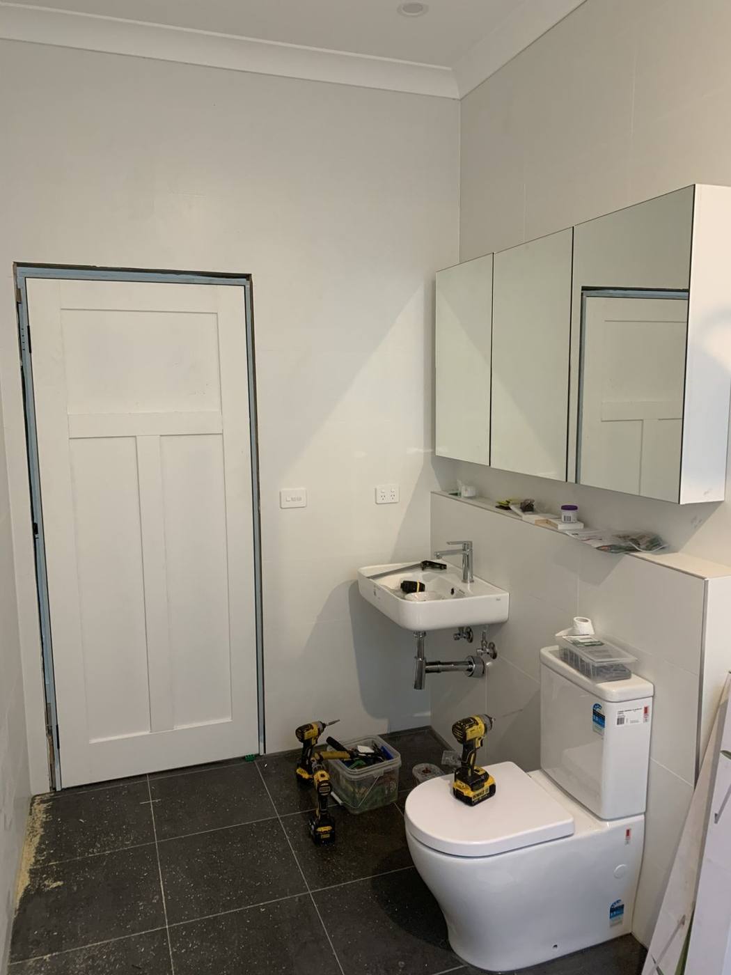 New bathroom during fit-out with wall-hung vanity and mirrored cabinet installed and tools on the floor, Dulwich Hill by Loel Homes