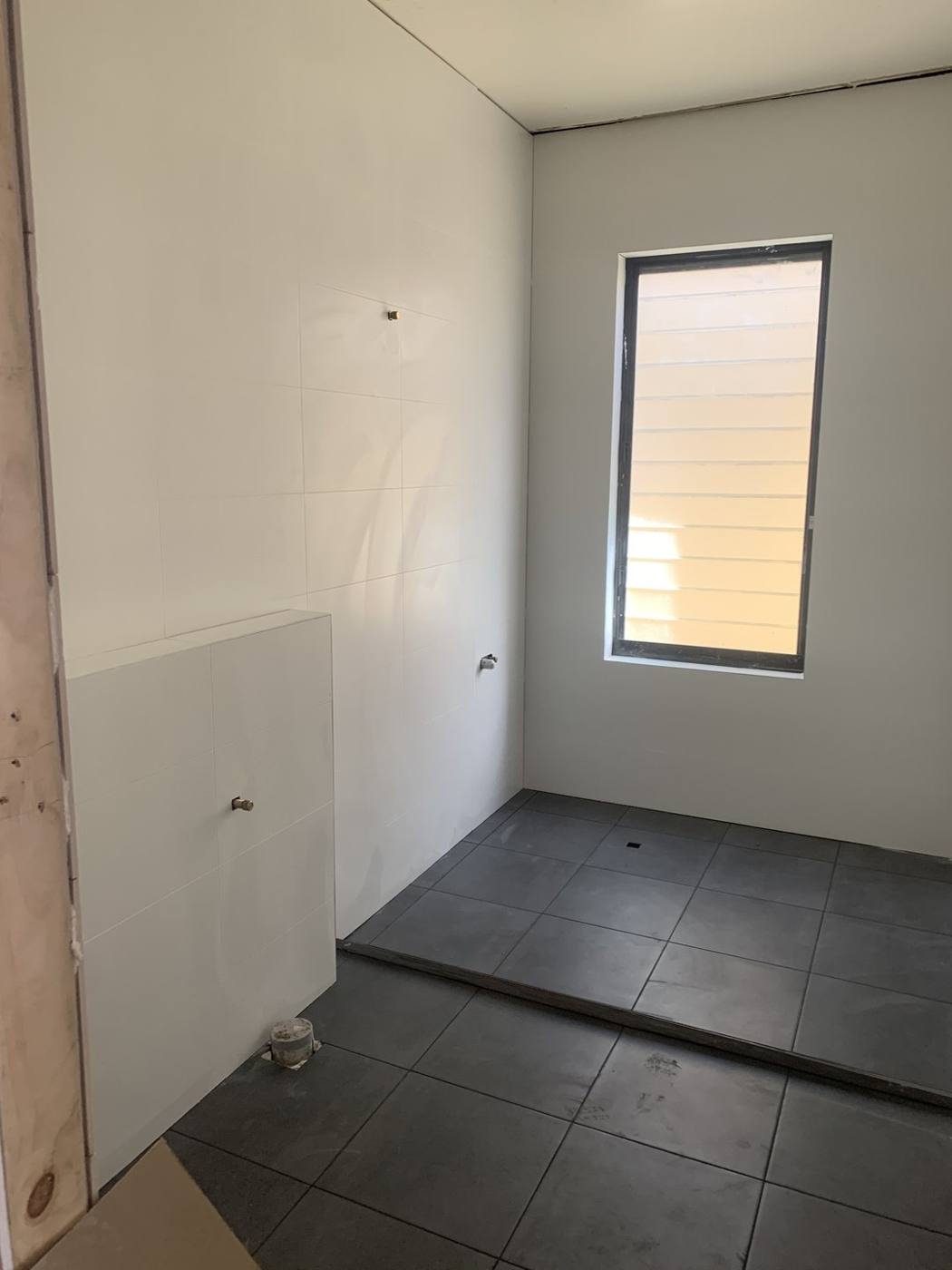 New bathroom tiled with white walls and charcoal floor tiles and tapware roughed in, before fittings and accessories, Dulwich Hill by Loel Homes