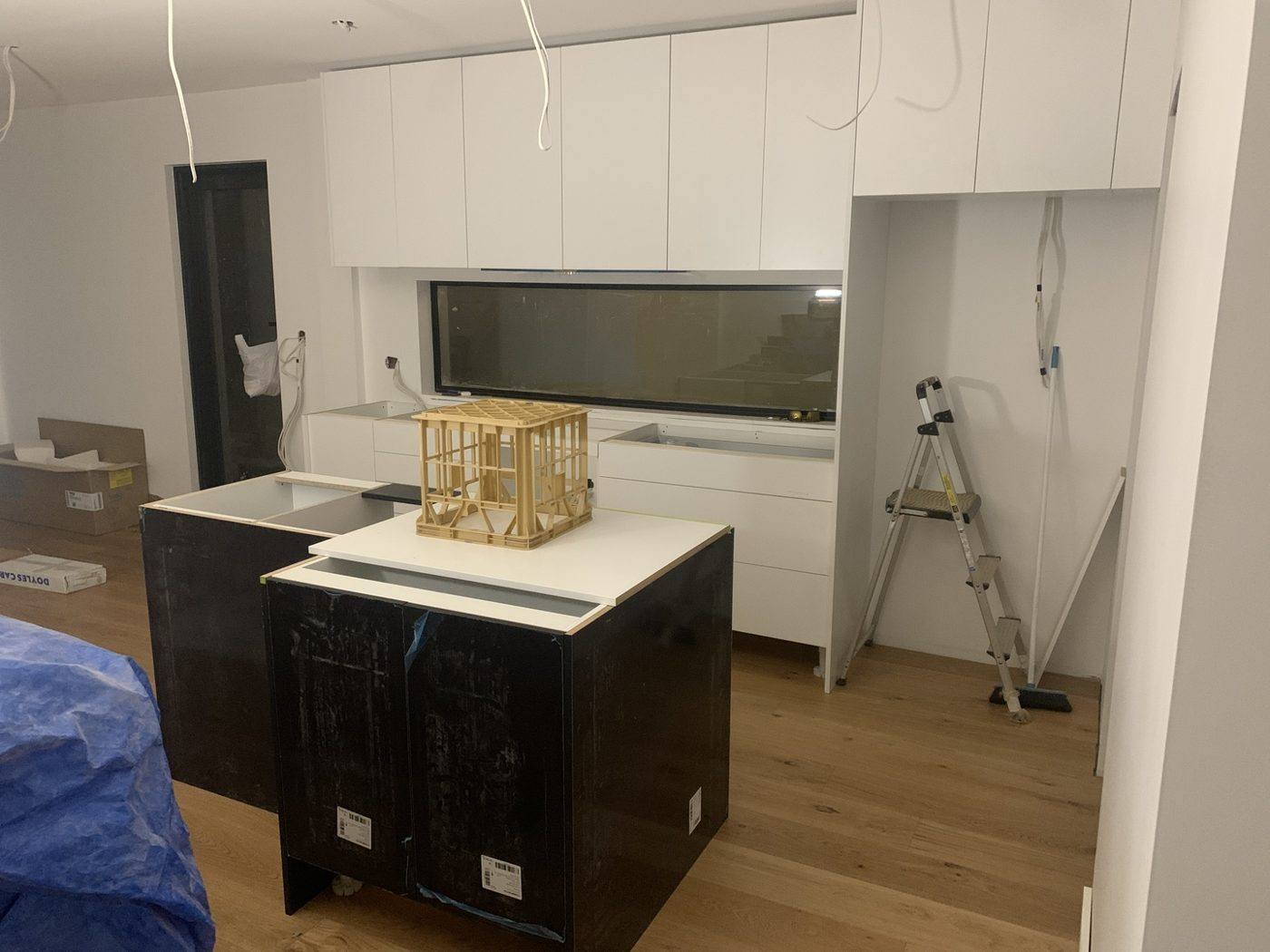 Kitchen with white overhead cabinetry, tall units and island base cabinets installed and protected, awaiting stone benchtops over timber floors, Dulwich Hill by Loel Homes