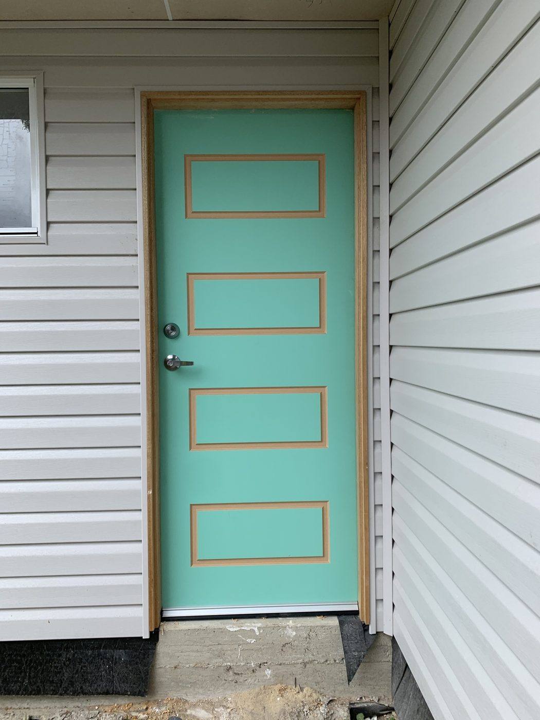Teal five-panel front entry door hung on a white weatherboard home by Loel Homes