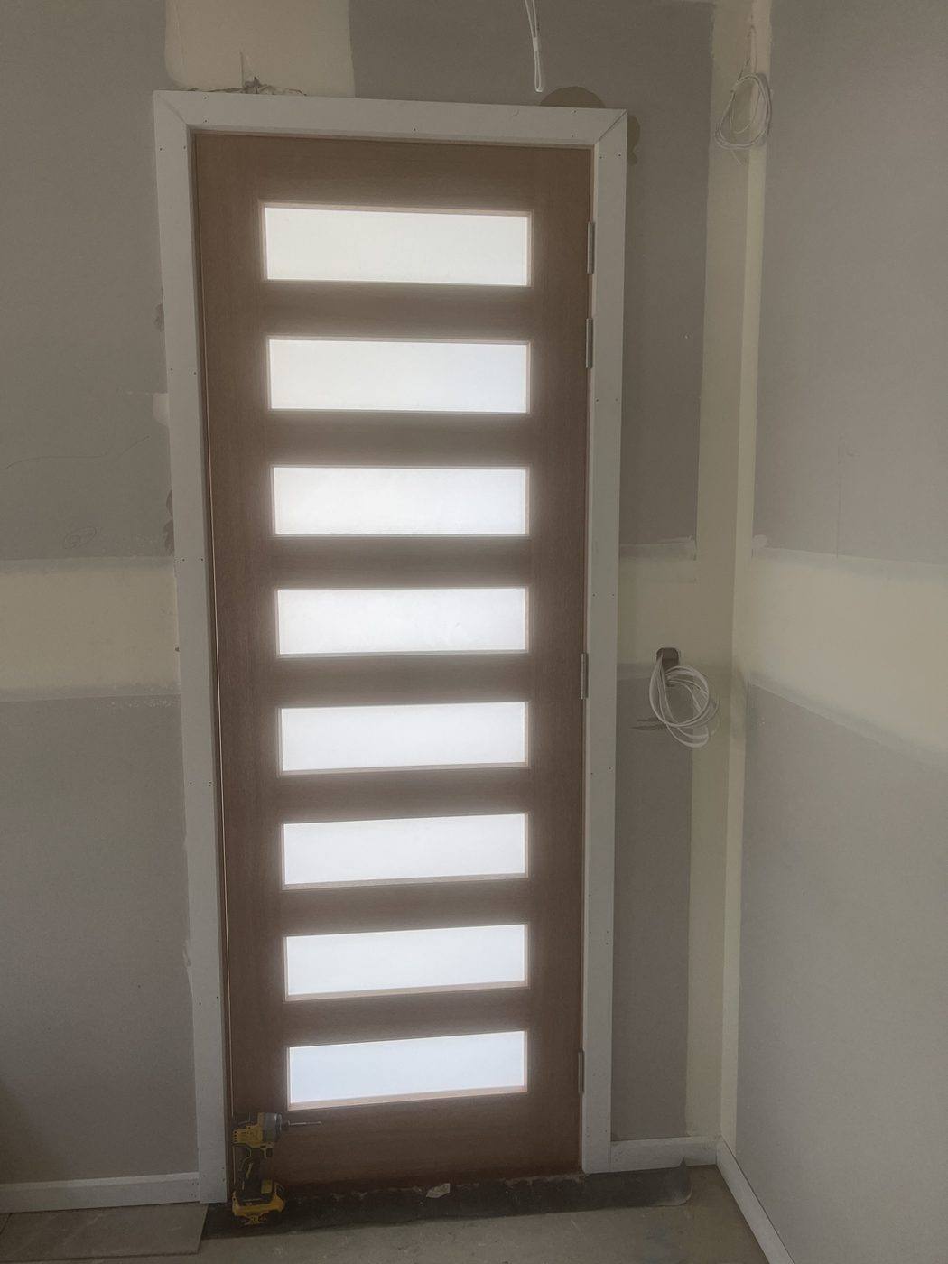 Same natural timber staggered-slot front entry door viewed from inside the hallway by Loel Homes