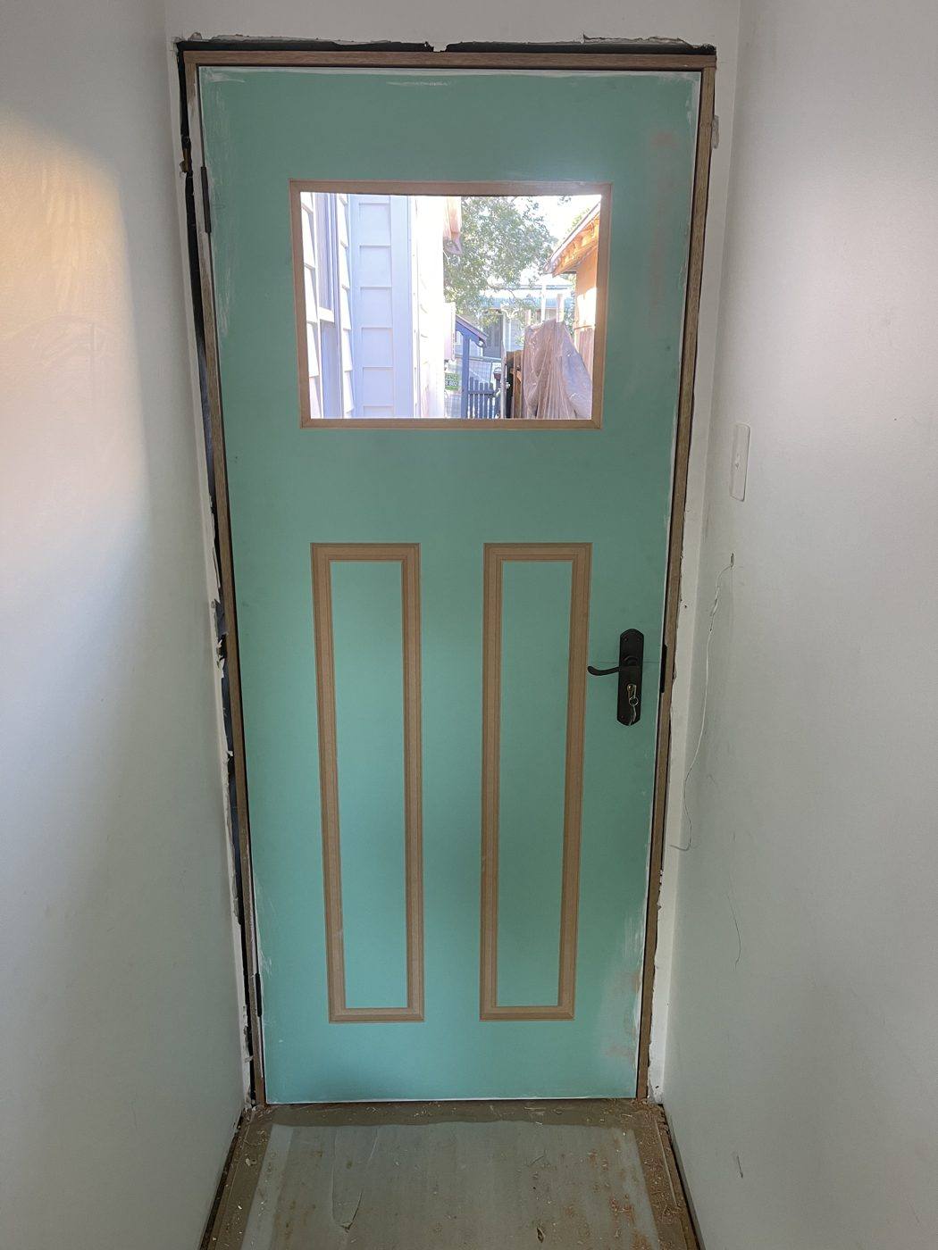 Teal front entry door with a vision panel window and colonial timber panels, viewed from inside by Loel Homes