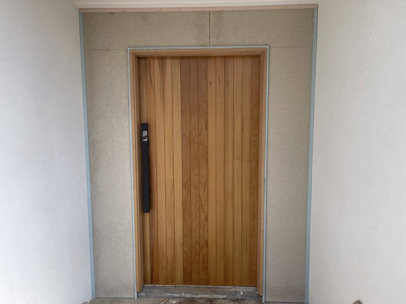 Finished oversized vertical-batten timber front entry door with electronic lock and full-height pull handle by Loel Homes