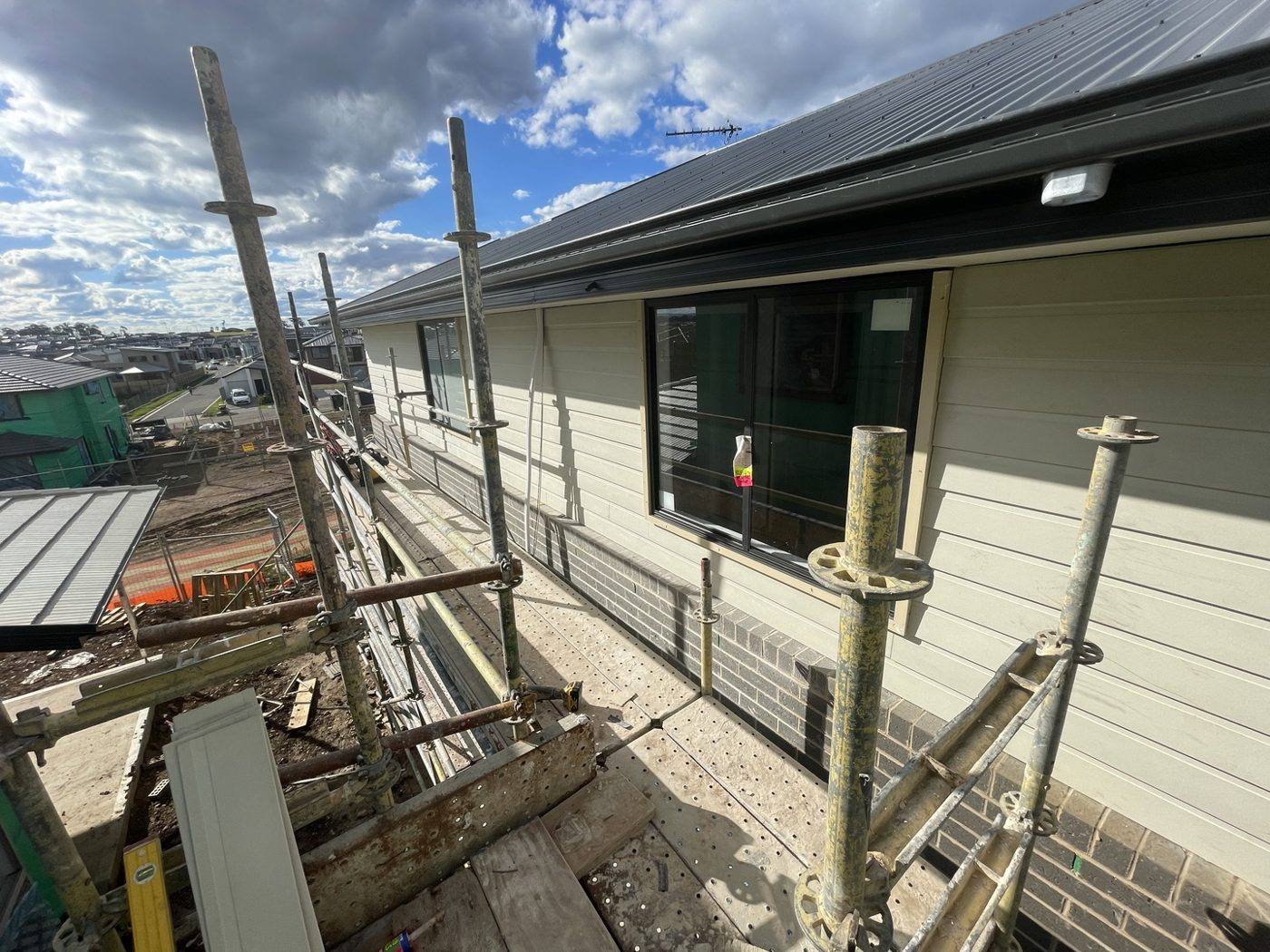 Upper-level elevation being clad in weatherboard with scaffold and site works below, double-storey home by Loel Homes