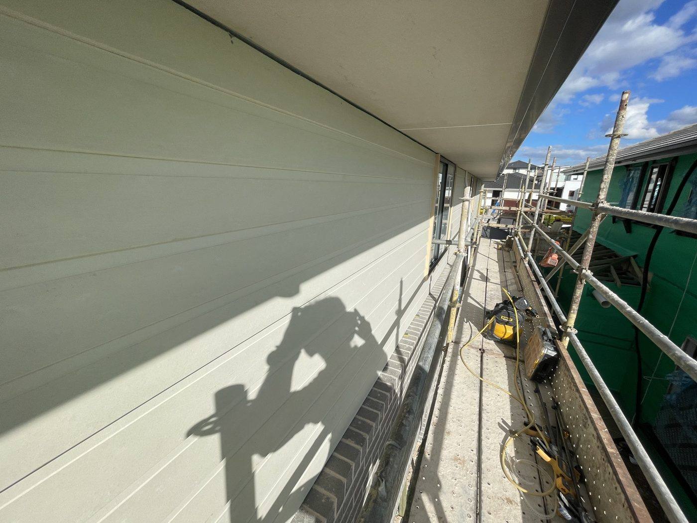 Worker sheeting the upper-level wall of a double-storey home with weatherboard cladding off scaffold, by Loel Homes