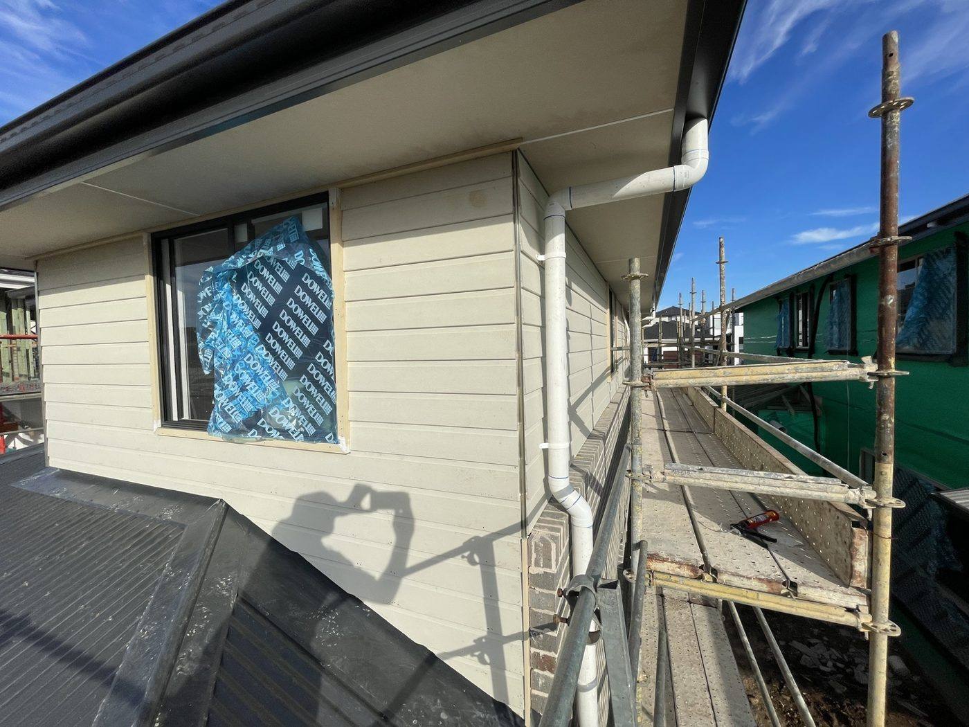 Upper-level window with wrap and downpipe during weatherboard cladding on a double-storey home, by Loel Homes