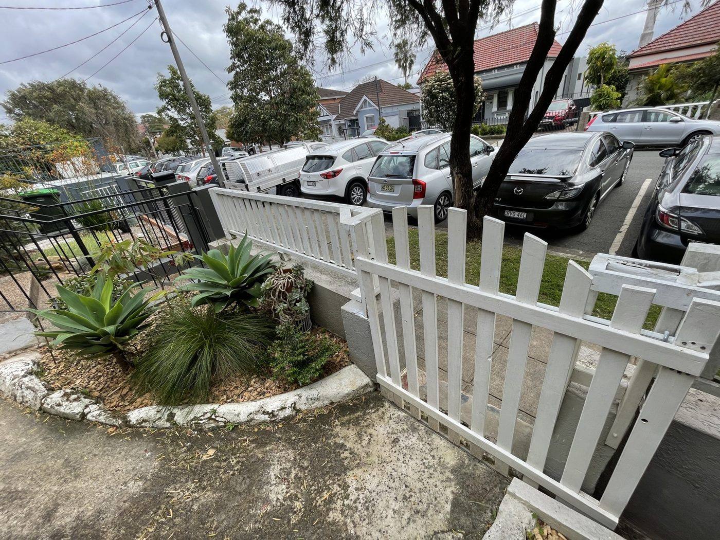 New rendered front garden bed with succulent planting behind a white picket fence by Loel Homes