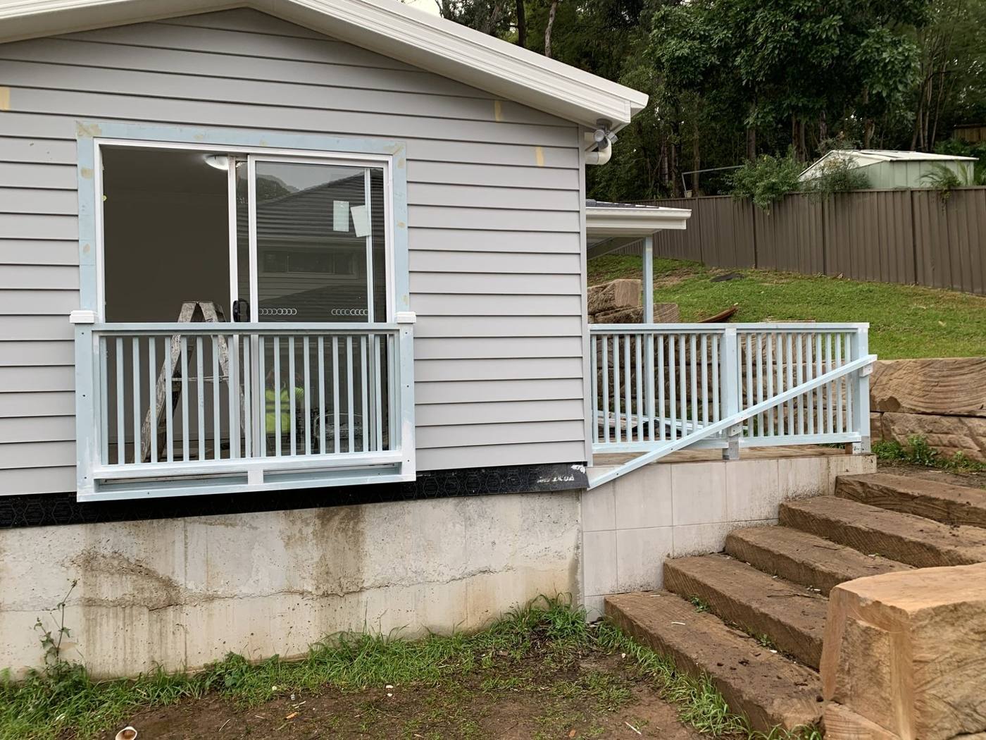 Finished Juliet balcony on a weatherboard home with white aluminium handrail and matching stone-block steps by Loel Homes