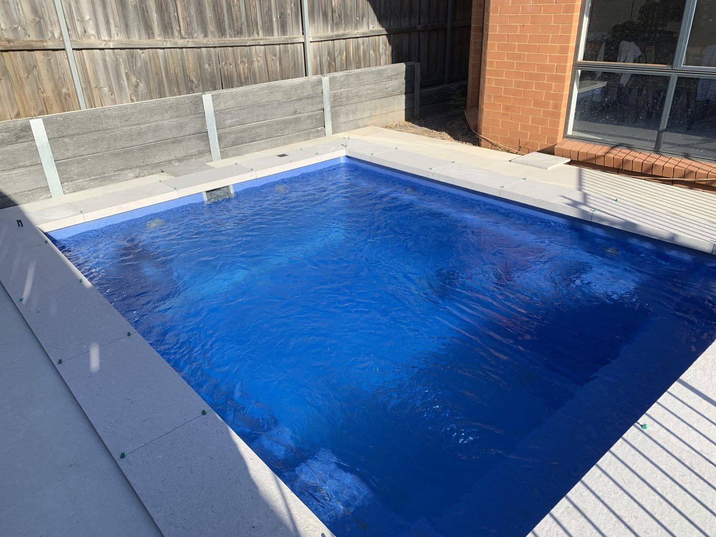 Newly filled backyard pool with coping done and temporary fence still in place by Loel Homes