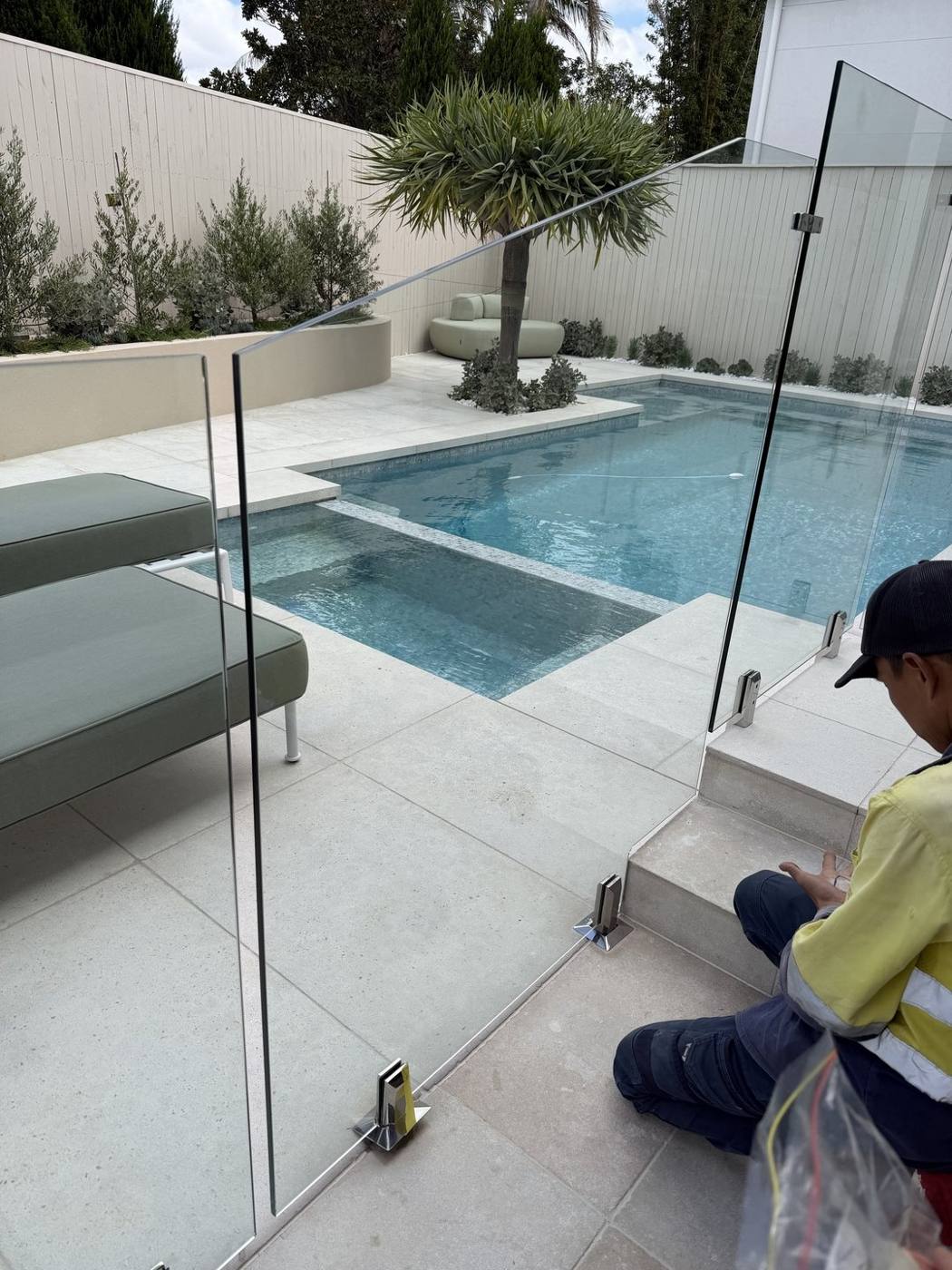 Frameless glass pool fencing being installed around a freeform pool by Loel Homes