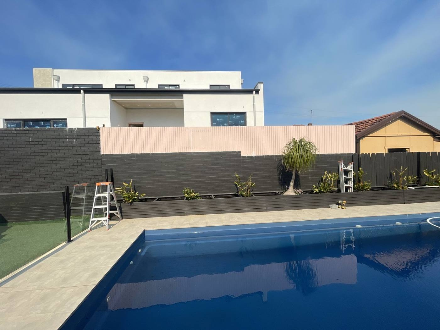 Finished pool with rendered feature wall, glass fencing and paved surround by Loel Homes