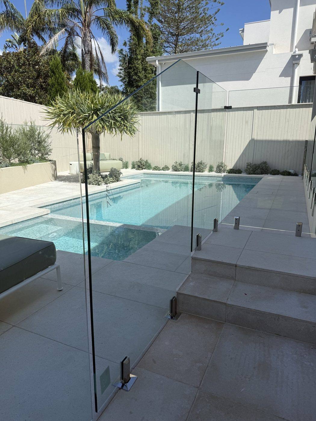 Finished freeform pool with frameless glass fencing, paved surround and landscaping by Loel Homes