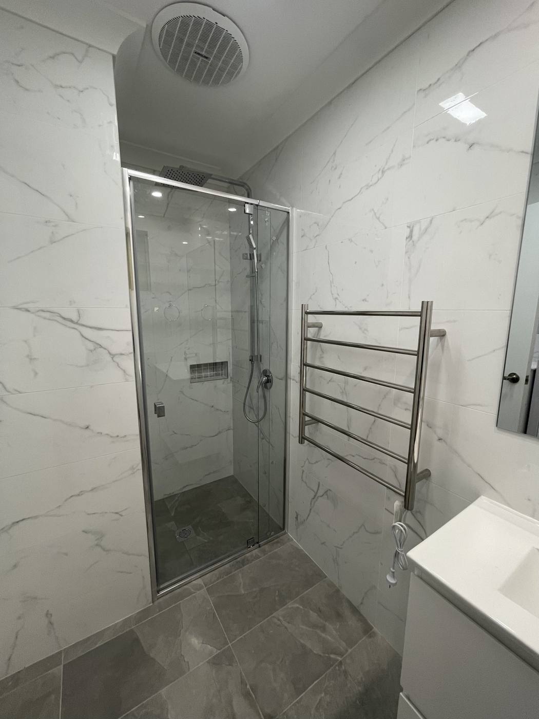 Finished frameless glass shower after renovation with rail shower, heated towel rail, marble-look wall tiles and grey stone-look floor, Quakers Hill by Loel Homes