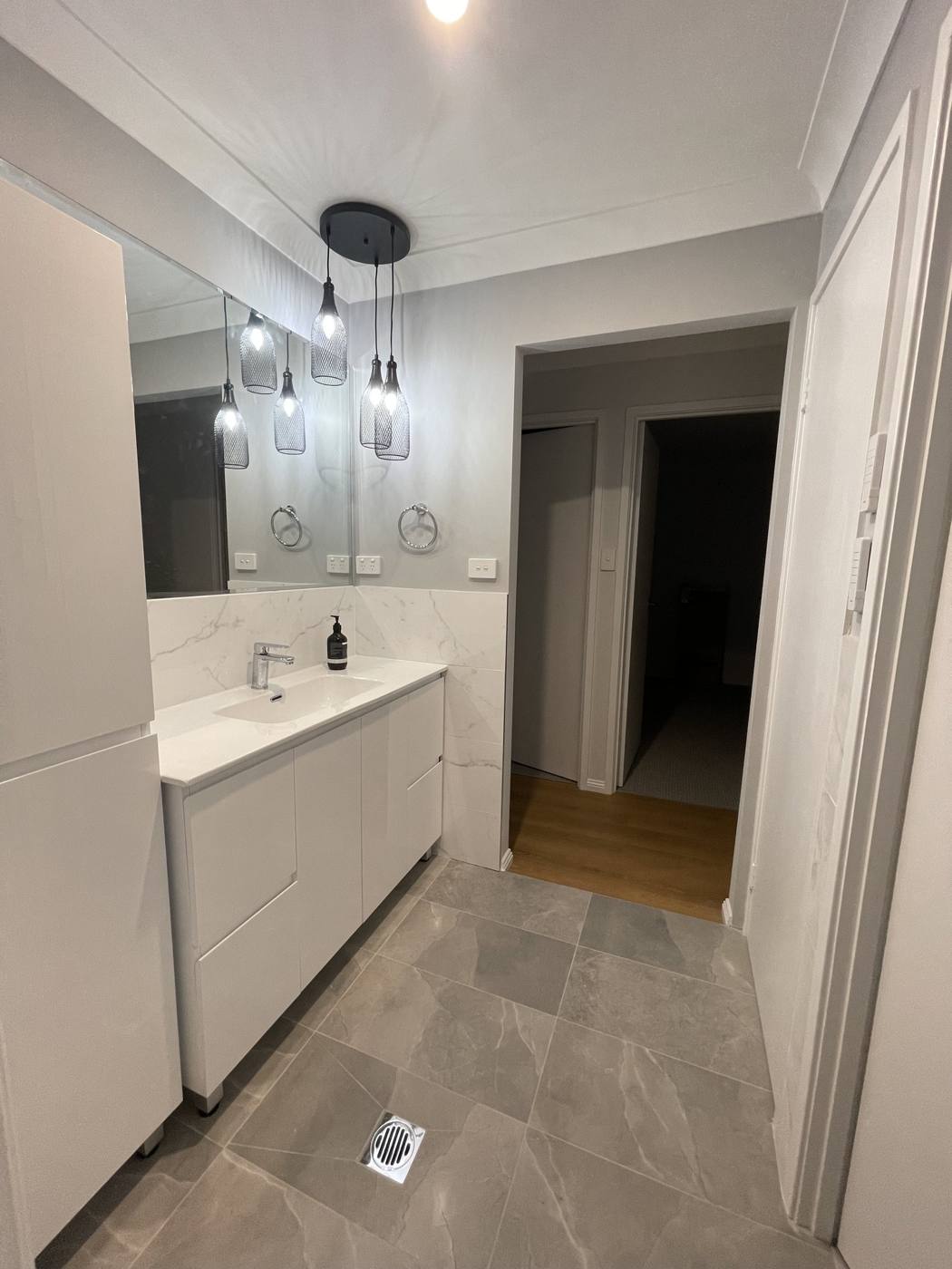 Finished bathroom after renovation looking past the white vanity and pendant lights to the hallway, grey stone-look floor tiles, Quakers Hill by Loel Homes