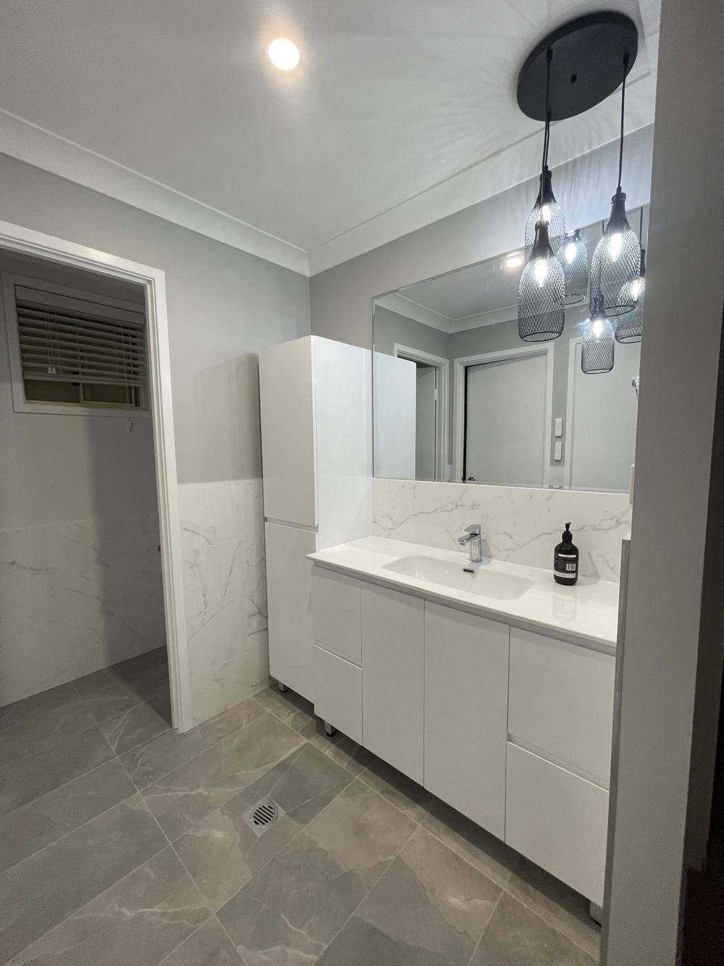 Finished bathroom after renovation with white shaker vanity, black wire cluster pendant lights, mirror cabinet and marble-look tiles, Quakers Hill by Loel Homes