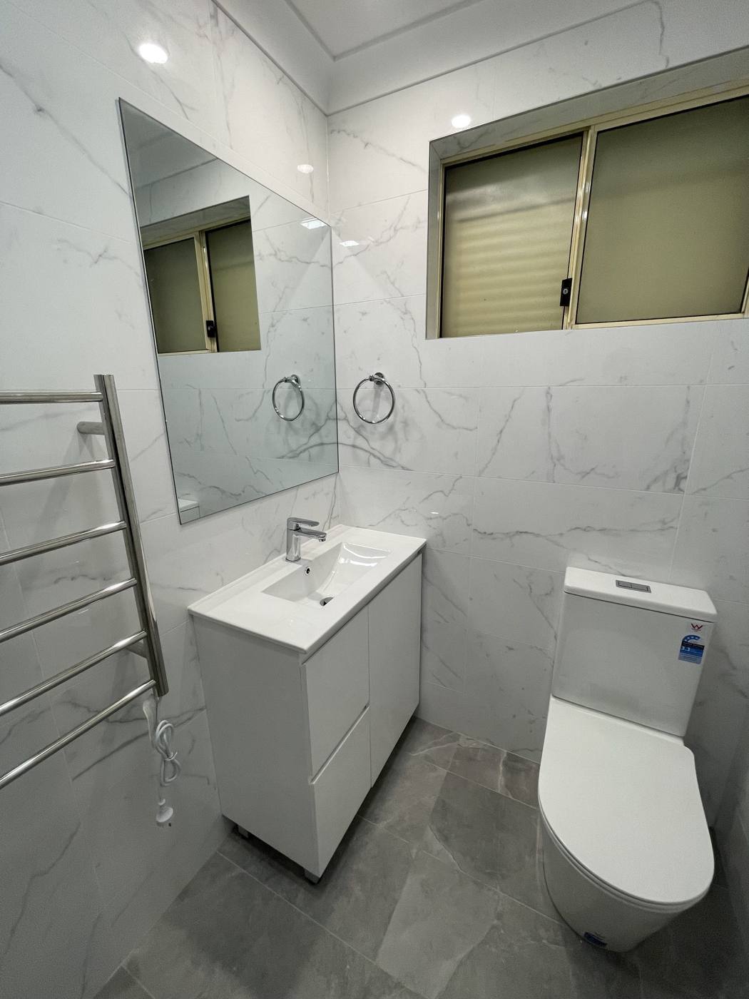 Finished bathroom after renovation with white vanity, mirror, heated towel rail, new toilet and marble-look wall tiles, Quakers Hill by Loel Homes