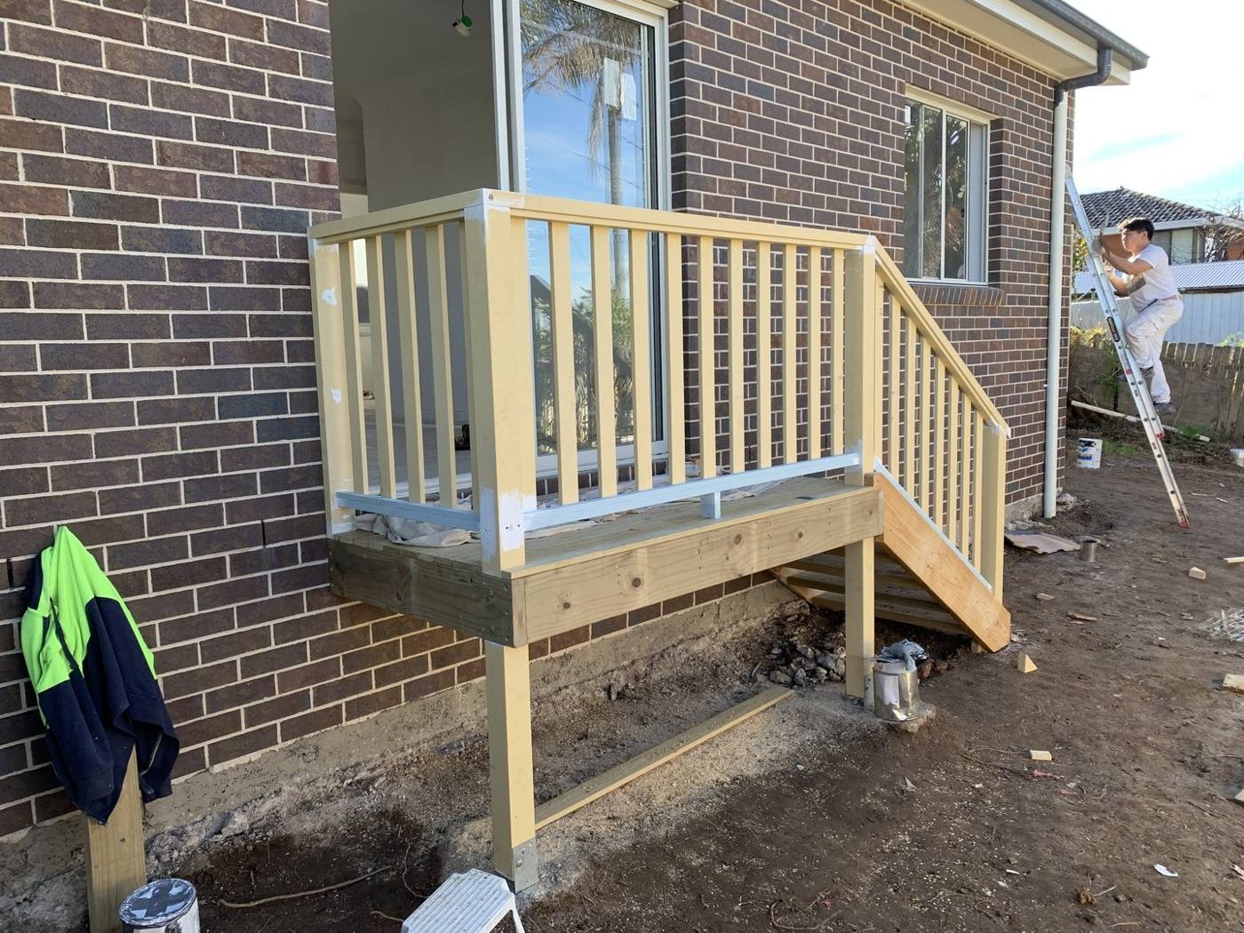 Timber balustrade going up on the raised deck with a painter on a ladder by Loel Homes