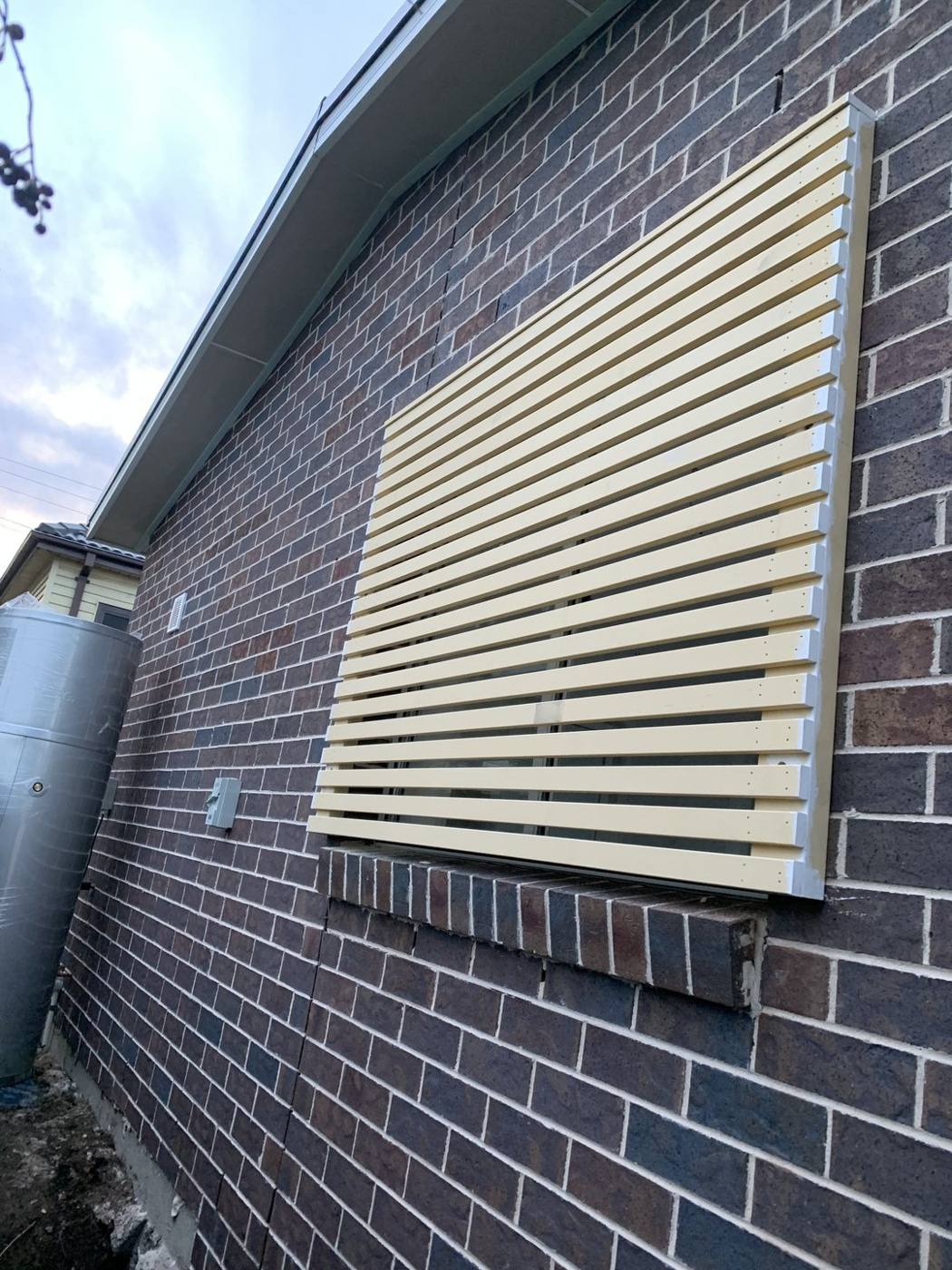 Beige aluminium slat privacy screen fixed to a brick wall by Loel Homes