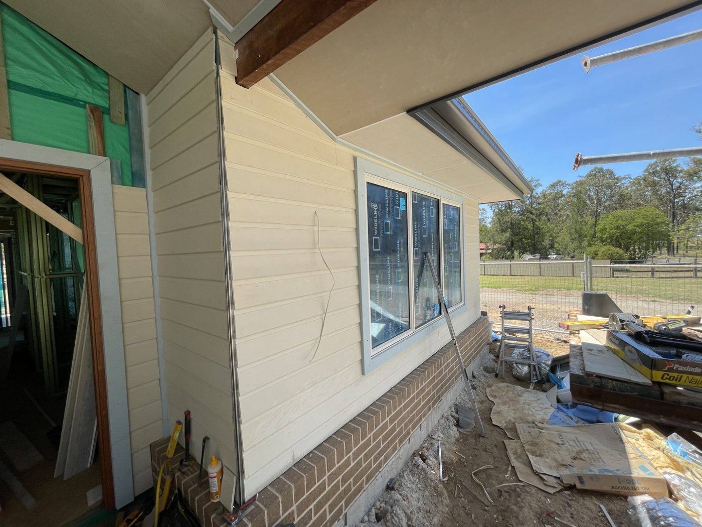 Side elevation fully clad in horizontal weatherboard above a brick base with windows installed, rural home by Loel Homes