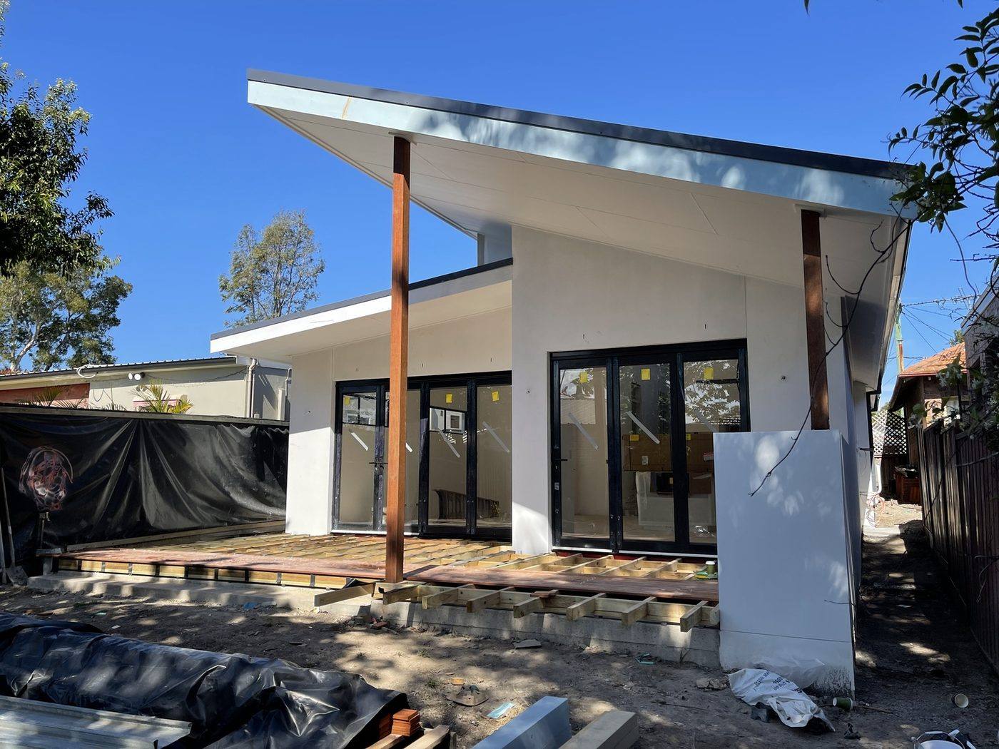 Rear skillion-roof extension with rendered walls, timber posts and black bi-fold doors, deck subframe being built, heritage terrace by Loel Homes
