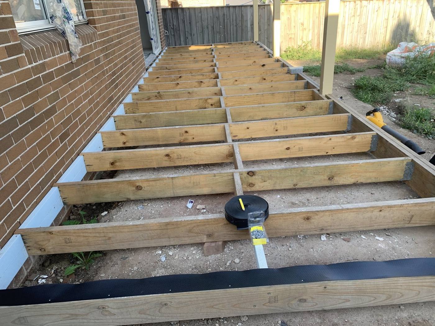 Timber deck joists and bearers set out against a red-brick wall by Loel Homes